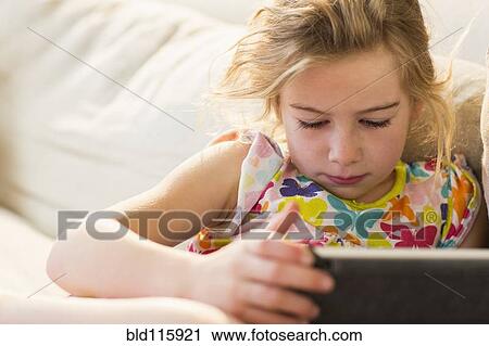 Stock Image - Caucasian girl using tablet computer on sofa. Fotosearch
