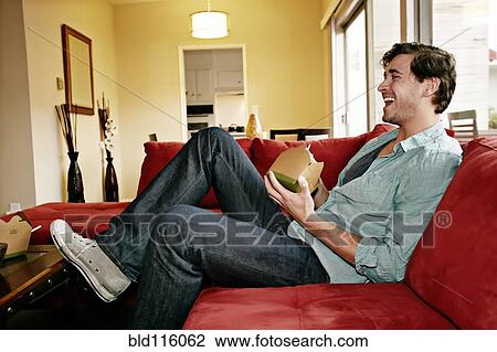 Stock Image - Caucasian man eating take out food on sofa. Fotosearch
