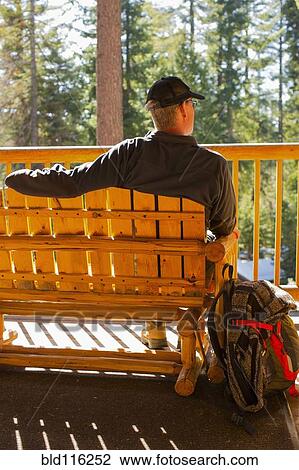 Stock Image - Caucasian man sitting on wooden bench. Fotosearch