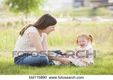 Stock Image - Caucasian mother and daughter playing in grass. Fotosearch