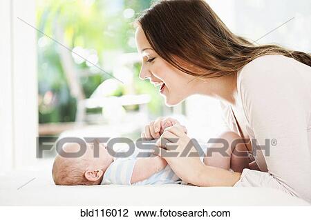 Stock Image - Caucasian mother playing with baby on changing table. Fotosearch