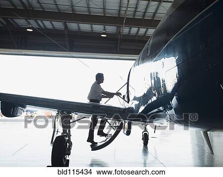 Picture - Caucasian pilot boarding airplane in hangar. Fotosearch