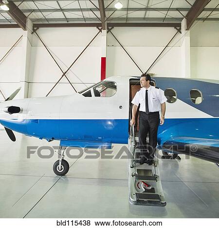 Stock Photo - Caucasian pilot disembarking airplane in hangar. Fotosearch