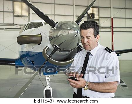 Stock Photo - Caucasian pilot using cell phone in hangar. Fotosearch