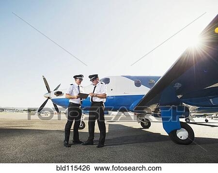Stock Photograph - Caucasian pilots using digital tablet on runway. Fotosearch