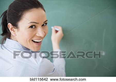 Stock Image - Caucasian teacher writing on blackboard. Fotosearch
