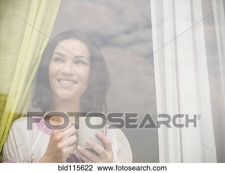 Stock Image - Caucasian woman drinking cup of coffee by window. Fotosearch