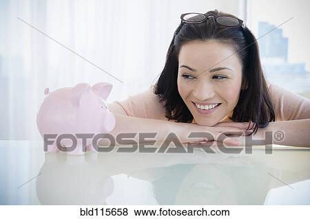 Stock Photo - Caucasian woman examining piggy bank. Fotosearch