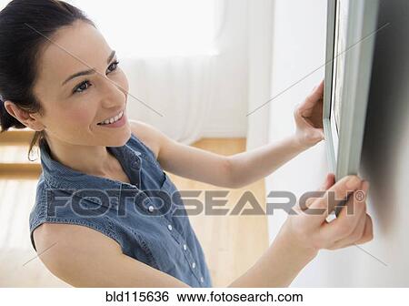 Stock Photograph - Caucasian woman hanging frame on wall. Fotosearch