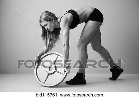 Stock Image - Caucasian woman lifting weight disc. Fotosearch
