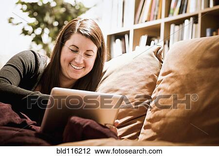 Stock Image - Caucasian woman using digital tablet on sofa. Fotosearch