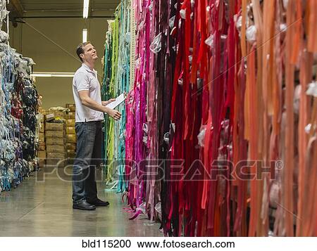 Stock Image - Caucasian worker examining fabric in textile factory. Fotosearch