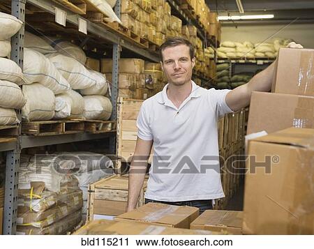 Stock Image - Caucasian worker stacking boxes in textile factory. Fotosearch