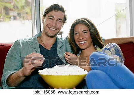 Stock Photo - Couple eating popcorn on sofa. Fotosearch