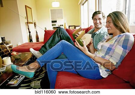 Stock Image - Couple eating take out food on sofa. Fotosearch