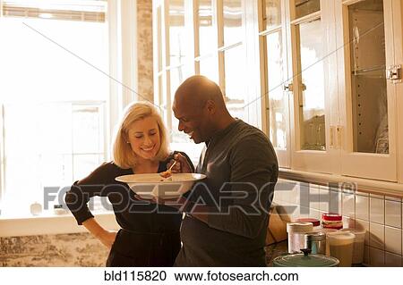 Stock Image - Couple sharing bowl of soup in kitchen. Fotosearch