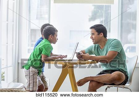 Stock Image - Father and sons talking at table. Fotosearch