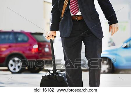 Stock Image - Hispanic businessman rolling luggage. Fotosearch