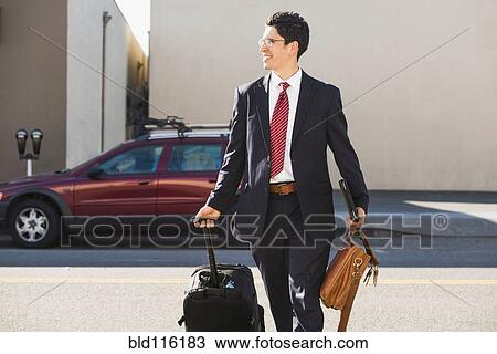 Stock Image - Hispanic businessman rolling luggage. Fotosearch