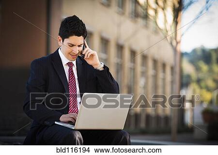 Picture - Hispanic businessman using laptop and cell phone. Fotosearch