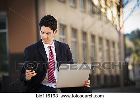 Stock Image - Hispanic businessman using laptop and cell phone. Fotosearch