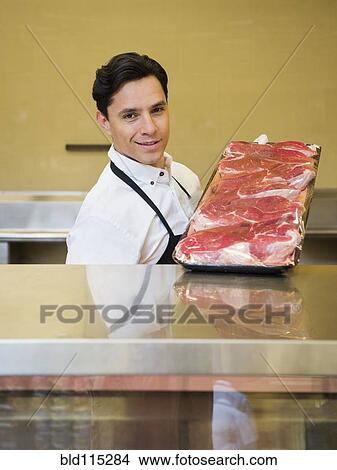 Picture - Hispanic butcher at meat counter of grocery store. Fotosearch
