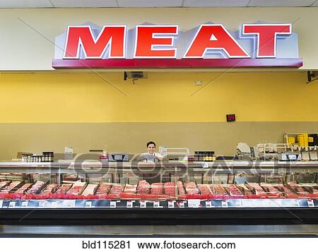Stock Image - Hispanic butcher at meat counter of grocery store. Fotosearch