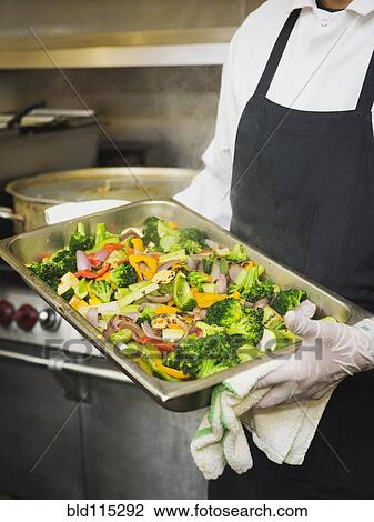 Stock Image - Hispanic chef with tray of vegetables in kitchen. Fotosearch