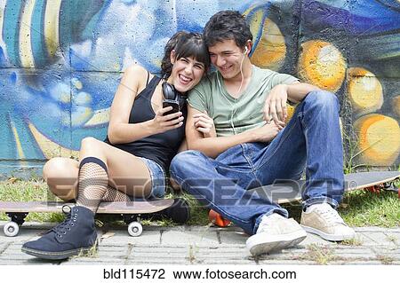 Stock Image - Hispanic couple sitting on skateboards. Fotosearch