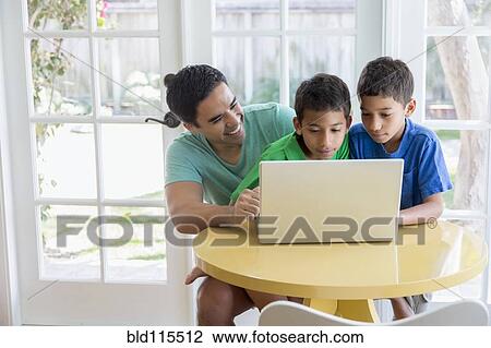 Stock Image - Hispanic father and sons using laptop. Fotosearch