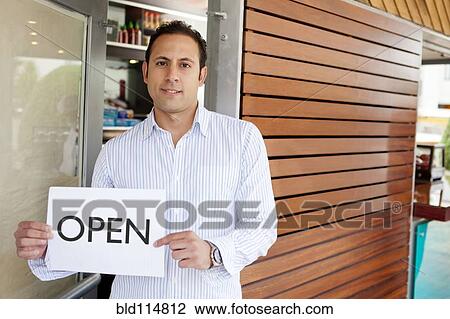 Stock Image - Hispanic man holding 'open' sign in door. Fotosearch
