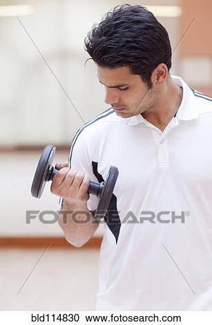 Stock Image - Hispanic man lifting weights in gym. Fotosearch