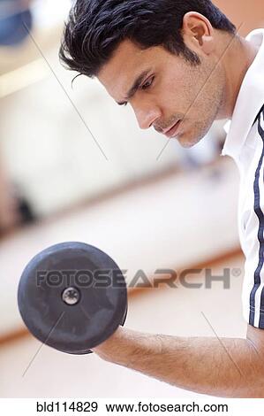 Stock Photo - Hispanic man lifting weights in gym. Fotosearch