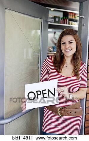 Stock Image - Hispanic woman holding 'open' sign in door. Fotosearch