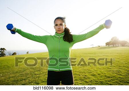 Stock Photo - Hispanic woman lifting weights in field. Fotosearch