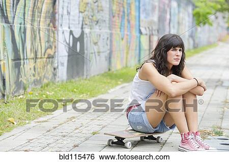 Stock Photograph - Hispanic woman sitting on skateboard. Fotosearch