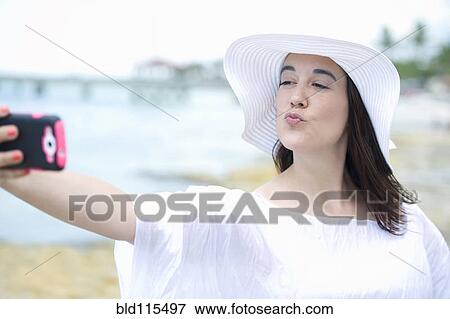 Stock Photo - Hispanic woman taking cell phone picture. Fotosearch