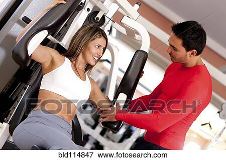 Stock Photo - Hispanic woman working with trainer in gym. Fotosearch