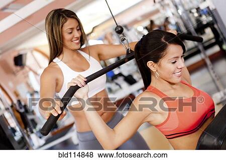 Stock Photo - Hispanic woman working with trainer in gym. Fotosearch