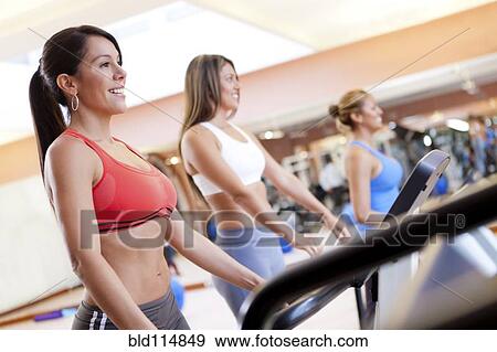 Stock Photo - Hispanic women using treadmills in gym. Fotosearch