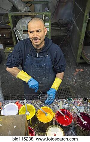 Stock Photo - Hispanic worker mixing paint in workshop. Fotosearch