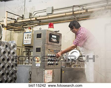 Stock Image - Hispanic worker operating machinery in textile factory. Fotosearch