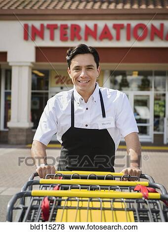 Hispanic worker pushing carts outside grocery store View Large Photo Image Stock Photo - Hispanic worker pushing carts outside grocery store. Fotosearch