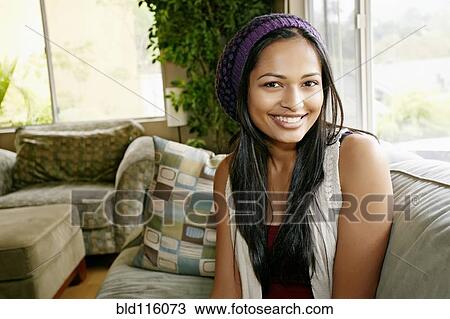 Stock Image - Indian woman smiling on sofa. Fotosearch