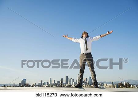 Stock Image - Mixed race businessman standing on urban rooftop. Fotosearch