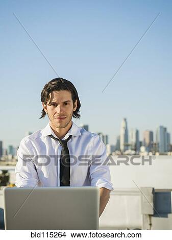 Picture - Mixed race businessman using laptop on urban rooftop. Fotosearch