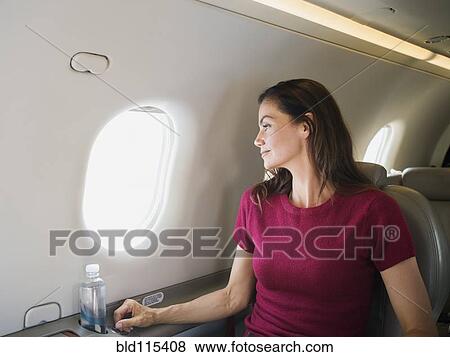 Stock Photo - Mixed race businesswoman looking out airplane window. Fotosearch
