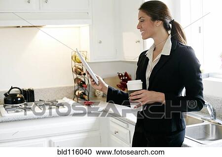 Stock Image - Mixed race businesswoman using tablet computer in kitchen. Fotosearch