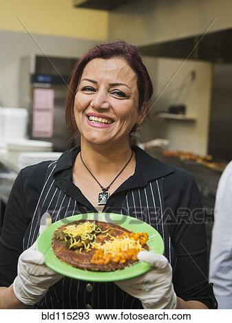 Stock Image - Mixed race chef holding plate of food in kitchen. Fotosearch