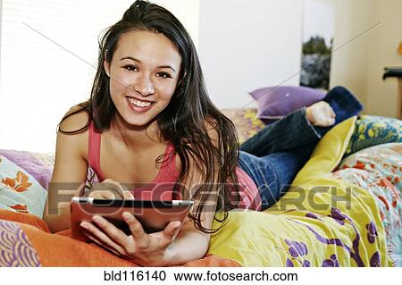 Stock Image - Mixed race college student using tablet computer in dorm. Fotosearch